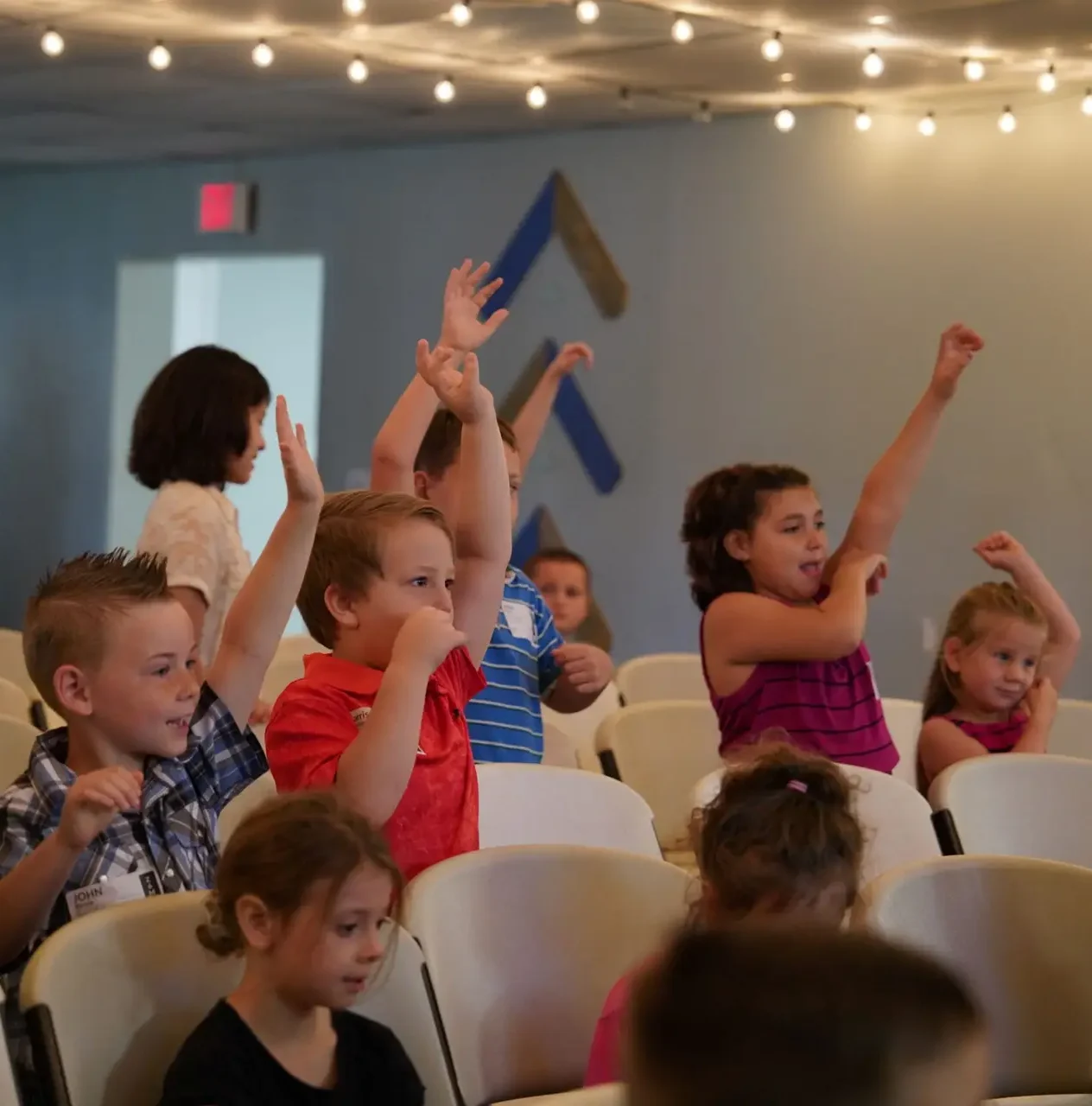 Children actively participating in Bethany Kids ministry with hands raised