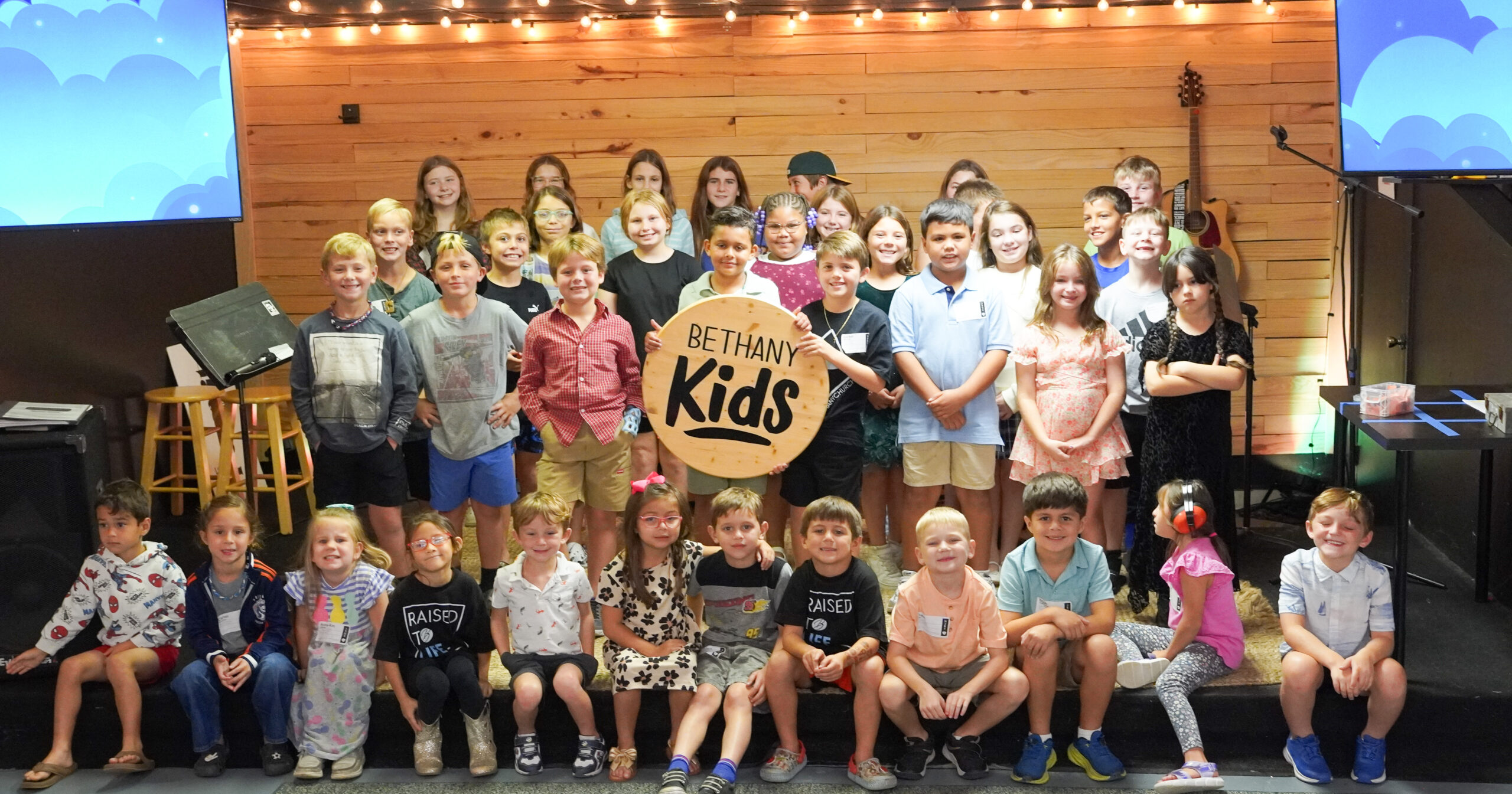 Children gathered together in Bethany Kids holding the ministry sign