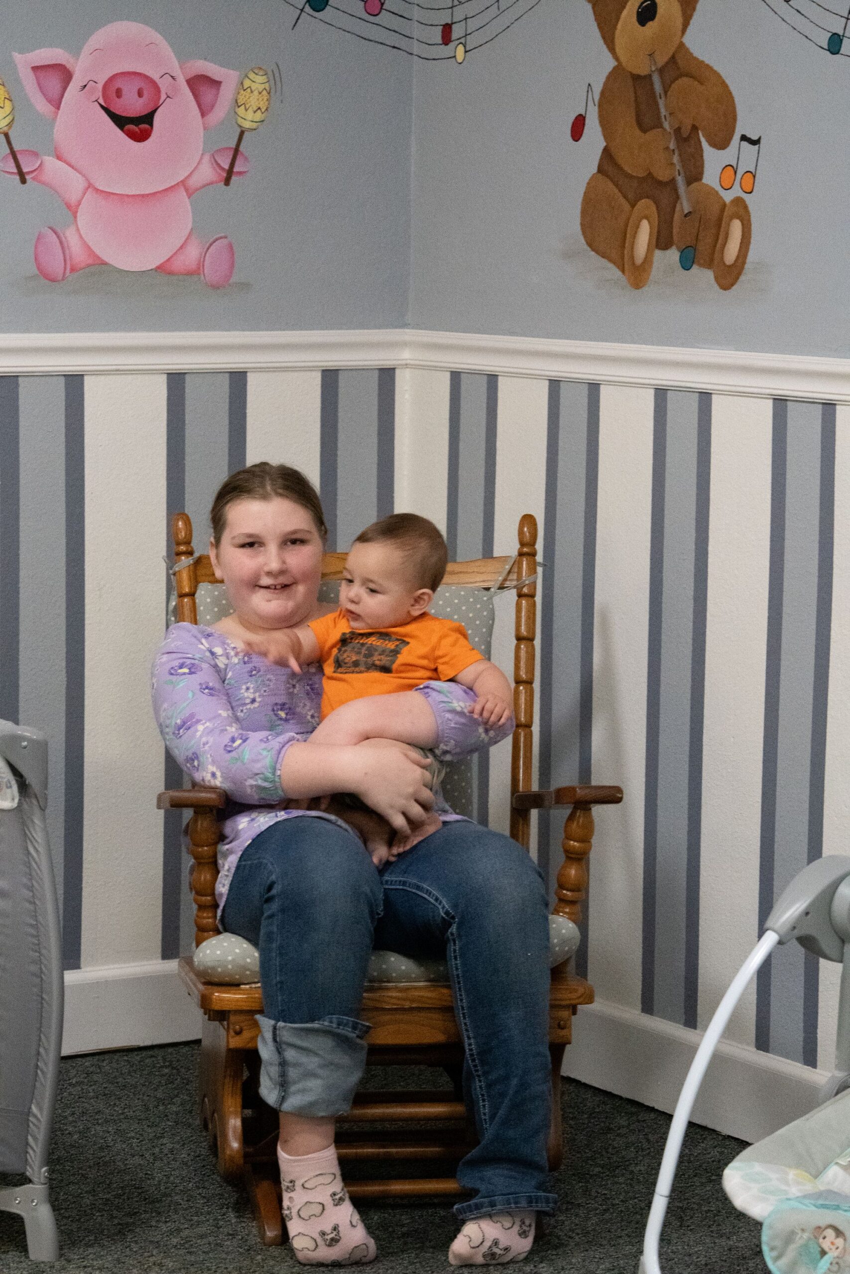 Child holding a baby in a nursery rocking chair in the Little Ones area