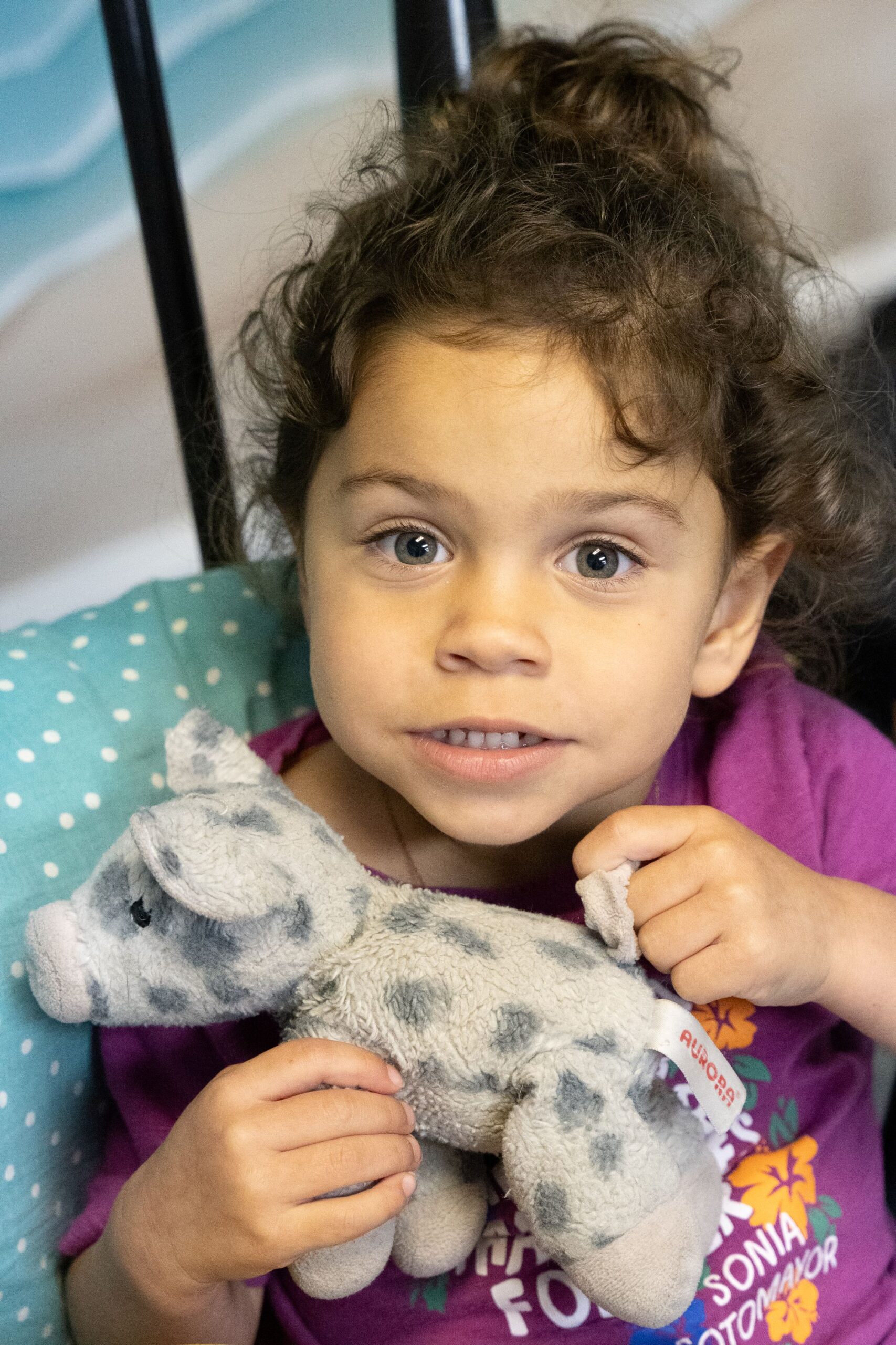 Young child smiling while holding a stuffed animal in the Little Ones room
